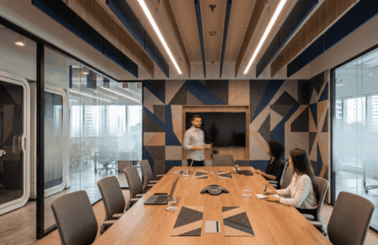 Sala de reuniões corporativa moderna com revestimento geométrico de painel acústico nas paredes em tons de azul e cinza, teto equipado com baffles e iluminação em LED, e profissionais ao redor de uma mesa de madeira.
